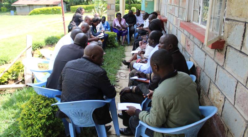 Members of the county technical team seated in rows outside a building during discussions