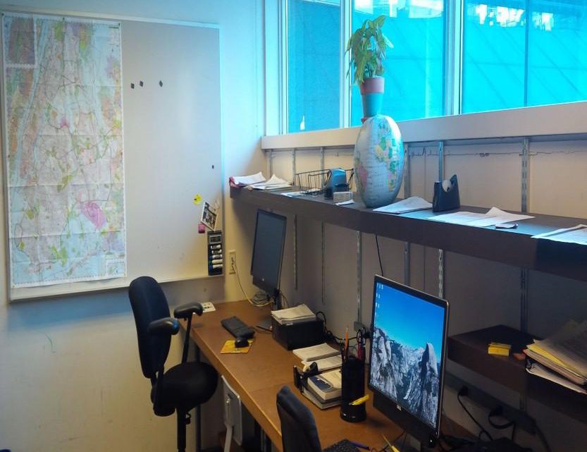 A small office with two monitors on a desk, a large map pinned to the wall and a globe on the window sill