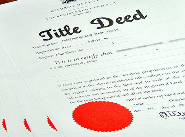 A stack of Kenyan title deeds, the top one showing its red seal and a signature, the title number partly obscured