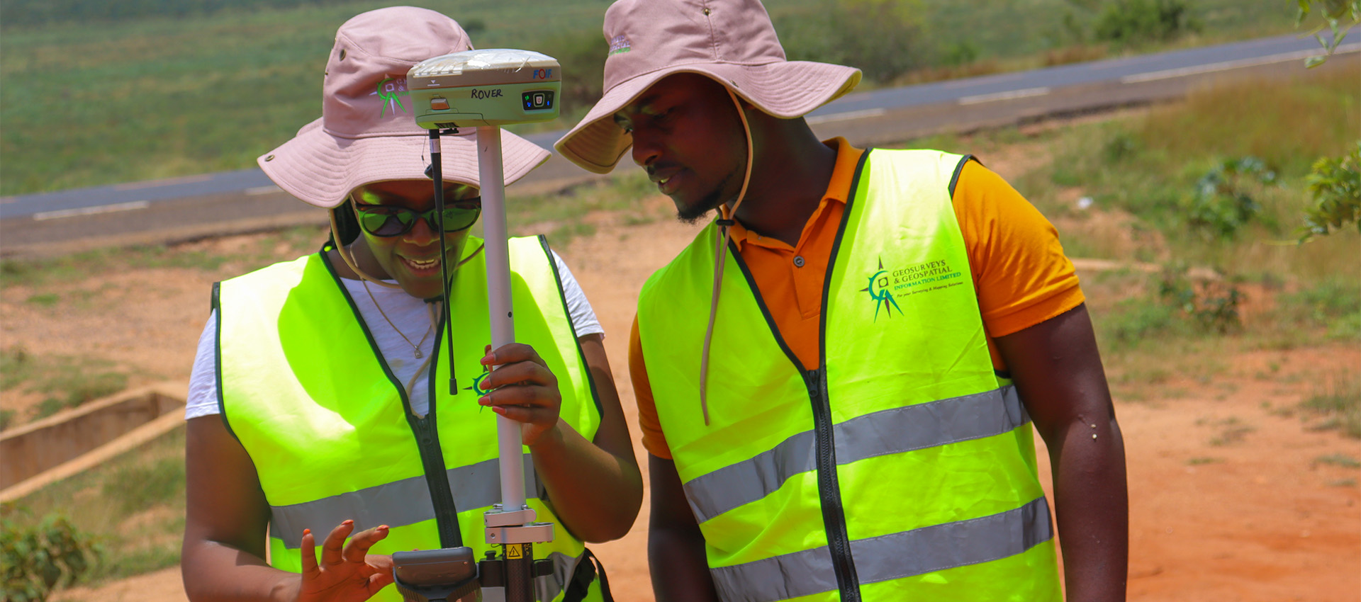 A GGIL field crew in hi-vis vests working with a GNSS rover on a murram road