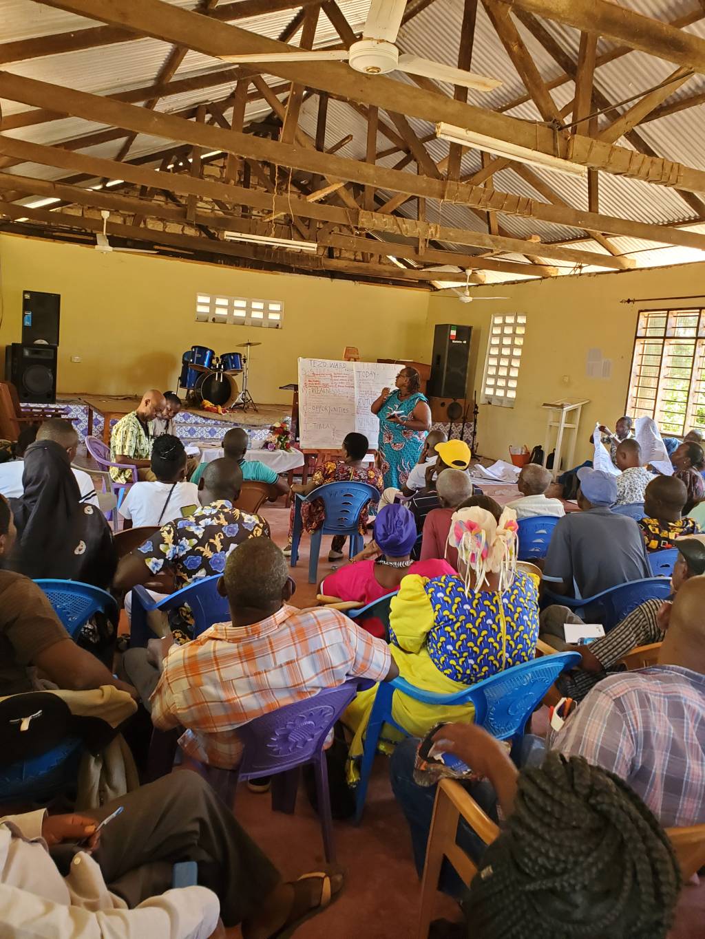 A crowded public participation session, residents seated in rows facing the front of a hall