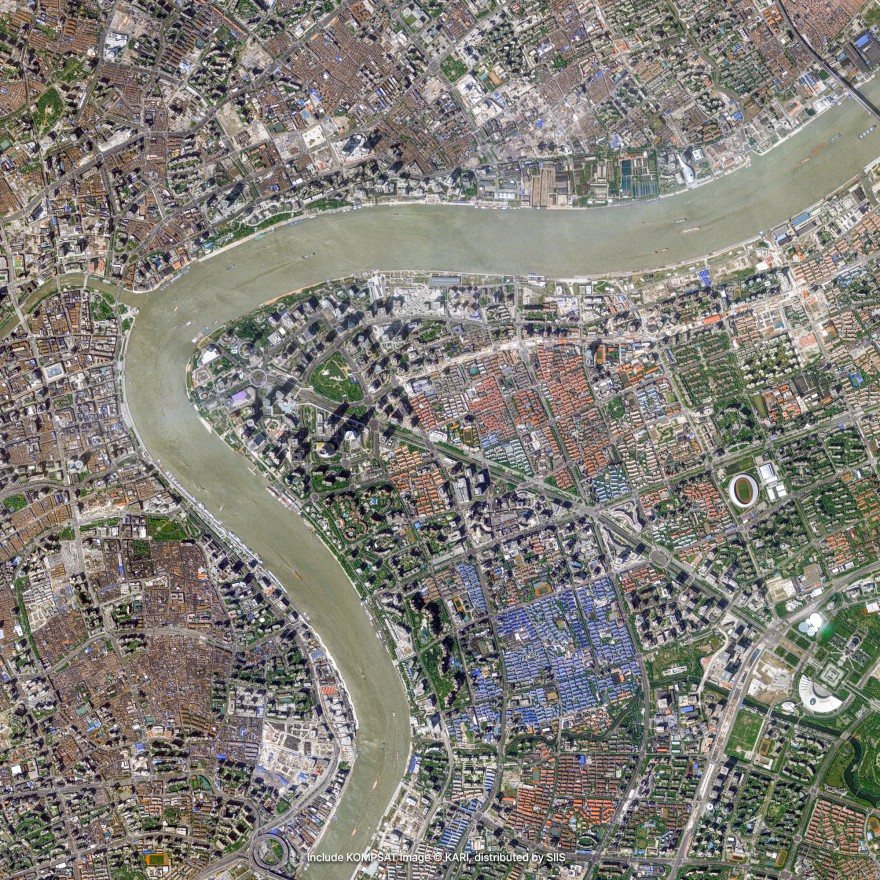 Satellite imagery of a large city on both banks of a wide river that bends through it, with dense blocks of buildings and a few parks
