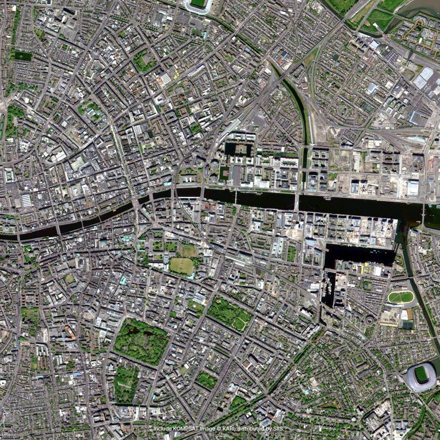 Satellite imagery of a dense city of streets and courtyards, crossed by a straight canal lined with docks, with a stadium at the lower right
