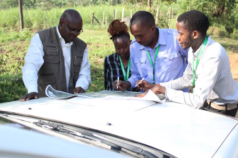 Members of the urban planning team examining a map spread on the bonnet of a vehicle